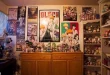 Rumah pop culture penuh koleksi action figure dan poster anime memenuhi dinding serta rak-rak kayu.