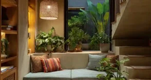 Sudut di bawah tangga dimanfaatkan jadi tempat duduk cozy dengan dekorasi tanaman dan pencahayaan hangat.